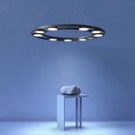 Lampa wisząca Fad LED, 9-punktowa, w kształcie okręgu, czarna z białymi kloszami, zawieszona na cienkich linkach. Tło w odcieniu niebieskim, lampa o nowoczesnym designie, umieszczona nad stołem z minimalistycznym elementem dekoracyjnym.