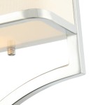 Kinkiet Gerdo Parette Cromo w chromowanej ramie, z beżowym abażurem. Ujęcie z bliska, pokazujące detal mocowania i kształt lampy. Elementy metalowe są błyszczące, a tło jest jasne, co podkreśla elegancki design.