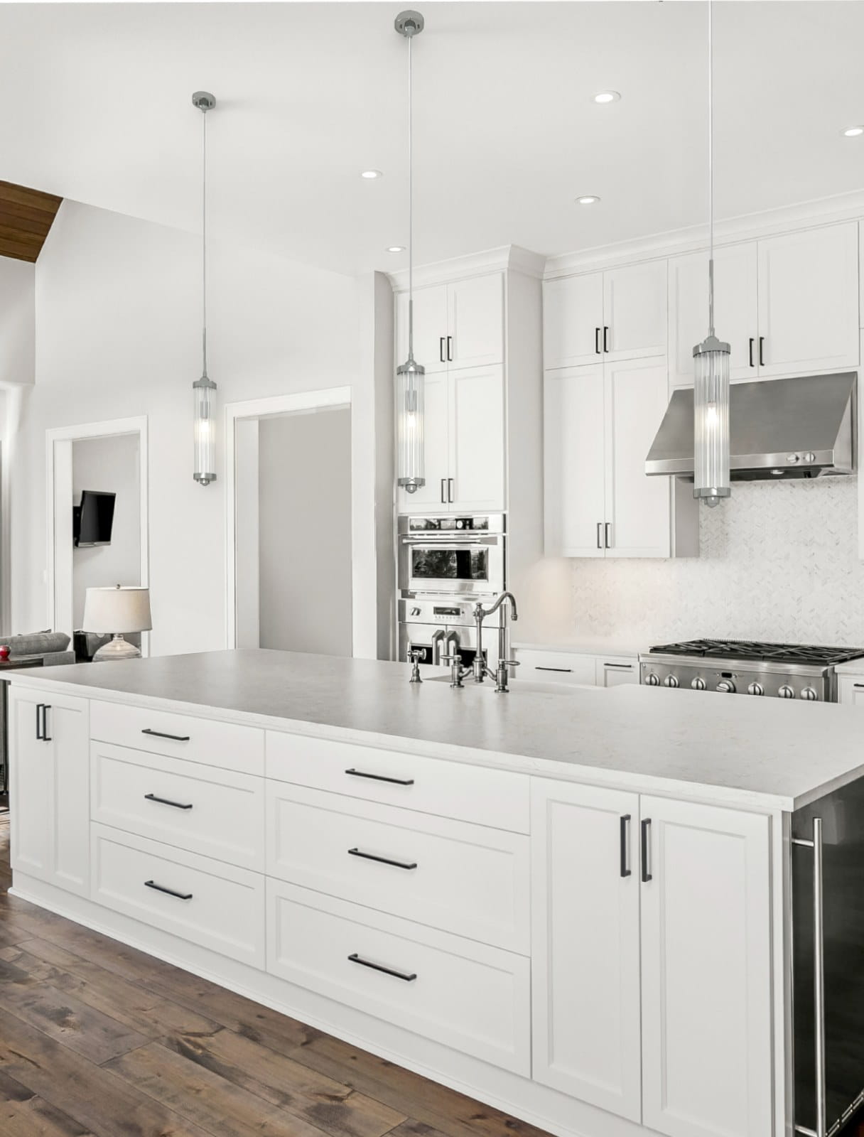 Lampa wisząca Fiatto I Cromo, jedno-punktowa, z chromowanym wykończeniem i szklanym kloszem w kształcie cylindrycznym. Zawieszona na cienkim kablu, w nowoczesnej kuchni z białymi szafkami i drewnianą podłogą.