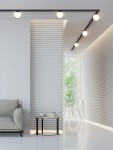 Czarny reflektor spot Track Movo zamontowany na szynie, emitujący ciepłe światło. Widoczny w nowoczesnym wnętrzu z białymi ścianami, szklanym oknem i minimalistycznym umeblowaniem. W tle kanapa i okrągły stół z dekoracjami.