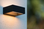 Goa LED kinkiet elewacyjny w kolorze czarnym, prostokątny, zamontowany na białej ścianie. Emituje ciepłe światło w dół, z widoczną metalową obudową i minimalistycznym designem. Idealny do oświetlenia zewnętrznego.