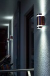 Kinkiet elewacyjny Focus 2-punktowy w kolorze inox, zamontowany na zewnętrznej ścianie. Oświetlenie emituje światło w górę i w dół, podkreślając fakturę ściany. Widoczny w kontekście oświetlonego korytarza.