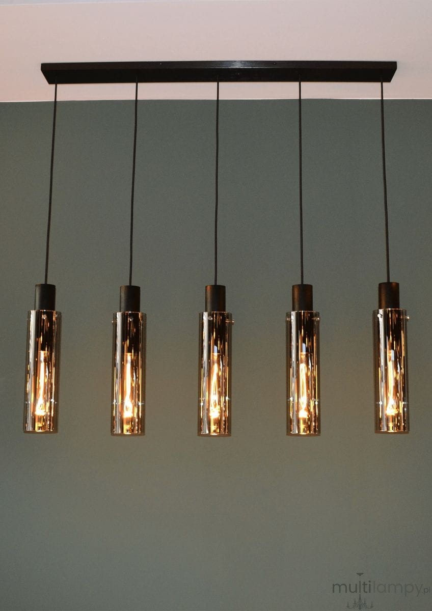 Czarna lampa wisząca Orlando z pięcioma punktami świetlnymi. Szklane klosze w cylindrycznym kształcie, zawieszone na czarnych przewodach. Lampa mocowana do sufitu za pomocą prostokątnej podstawy. Tło w odcieniu zieleni.