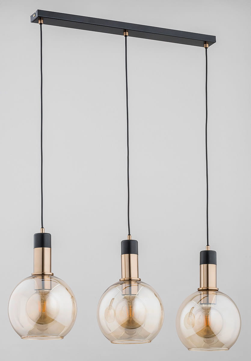 Lampa wisząca Maya 3-punktowa w złotym kolorze. Składa się z trzech okrągłych kloszy z przezroczystego szkła, zawieszonych na czarnych przewodach, umocowanych na prostokątnej, czarnej podstawie.