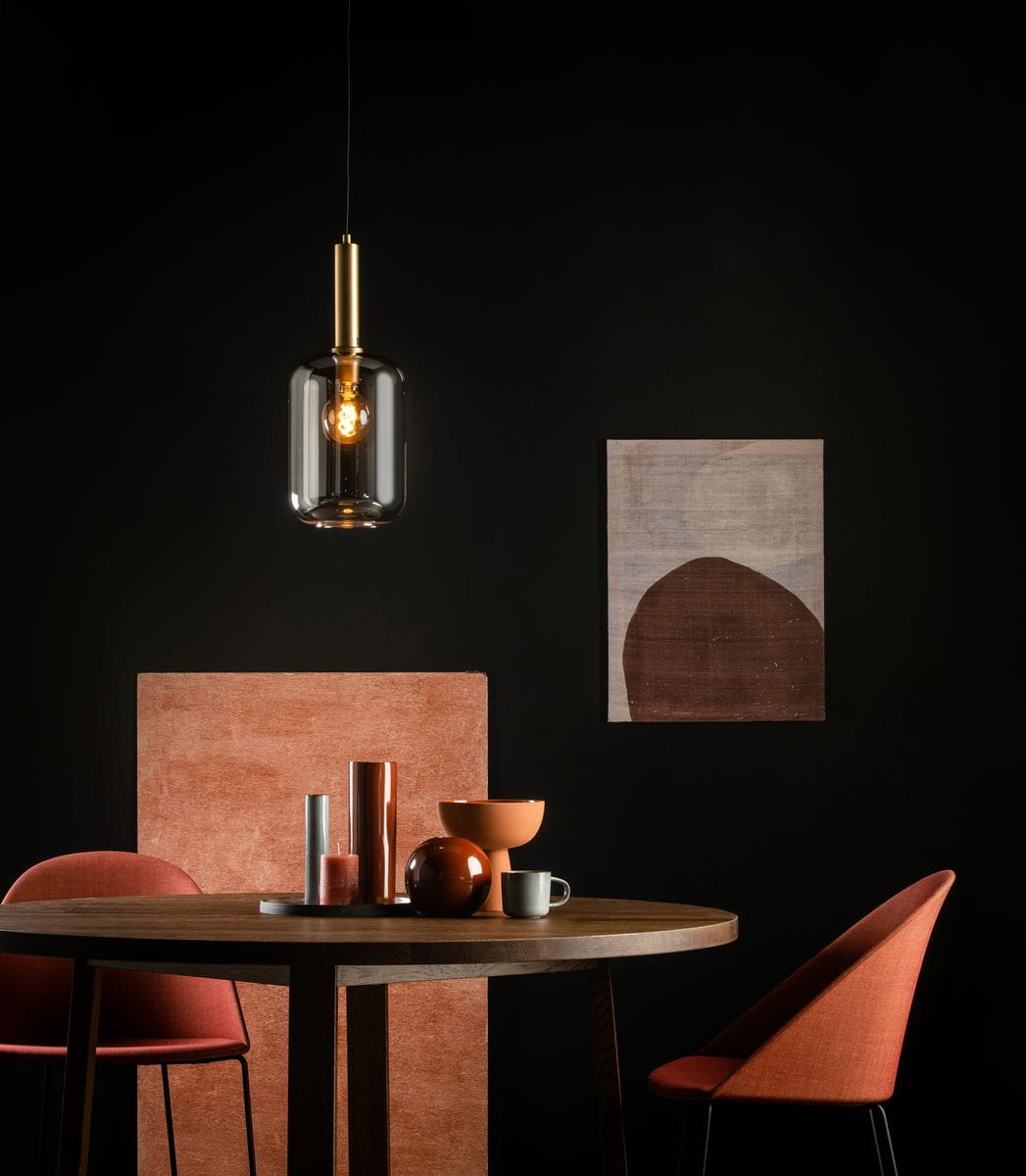Lampa wisząca Joanet 1-punktowa w kolorze czarnym z metalowym, złotym uchwytem. Szklany klosz z przezroczystym wykończeniem. Zawieszona nad okrągłym drewnianym stołem, w otoczeniu rustykalnych elementów dekoracyjnych i czerwonych krzeseł.