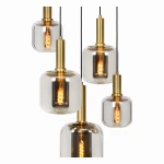 Lampa wisząca Joanet 5-punktowa w kolorze czarnym, z pięcioma szklanymi kloszami w różnych kształtach, zawieszonymi na czarnych kablach. Metalowe elementy w kolorze złotym, widoczne żarówki z dekoracyjnym filamentem.