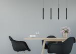 Czarna lampa wisząca LED Lorenz 4-punktowa, składająca się z czterech smukłych, cylindrycznych kloszy, zawieszona nad drewnianym stołem w minimalistycznym wnętrzu. Tło w jasnoszarym kolorze, z kwiatami w wazonie i naczyniami na stole.
