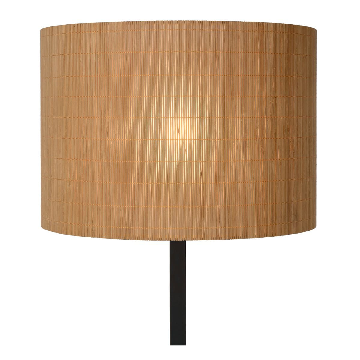 Lampa podłogowa Magius o czarnym stelażu, z okrągłym kloszem w naturalnym kolorze, wykonanym z cienkich pasków materiału. Ujęcie frontalne, lampa stoi na podłodze, emitując ciepłe światło przez klosz.