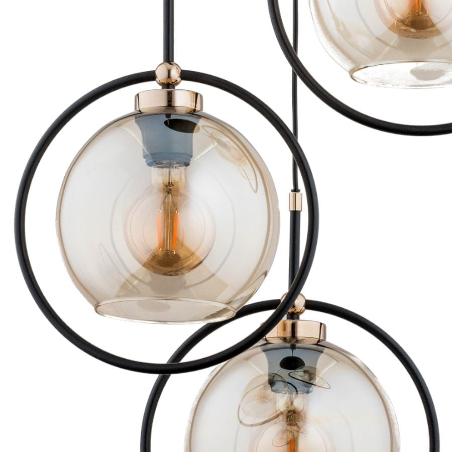 Lampa wisząca Seldi 3-punktowa w kolorze czarnym i złotym. Składa się z trzech szklanych kloszy w kształcie kul, zamocowanych w metalowych pierścieniach. Widoczna żarówka w centralnej części każdego klosza, w otoczeniu cienkiego przewodu.