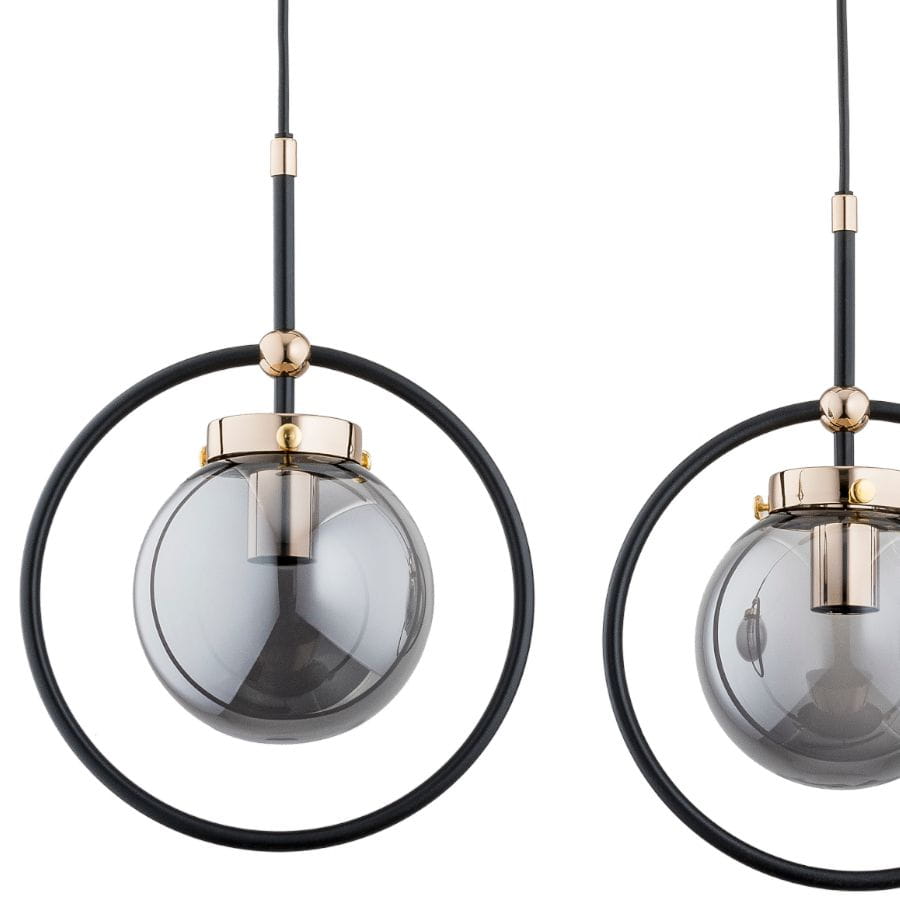 Lampa wisząca Akira 3-punktowa w kolorze czarnym i złotym. Składa się z trzech szklanych kul w dymnym odcieniu, osadzonych w metalowych pierścieniach. Kable montażowe w kolorze czarnym, wykończenia w złotym kolorze. Ujęcie frontalne.