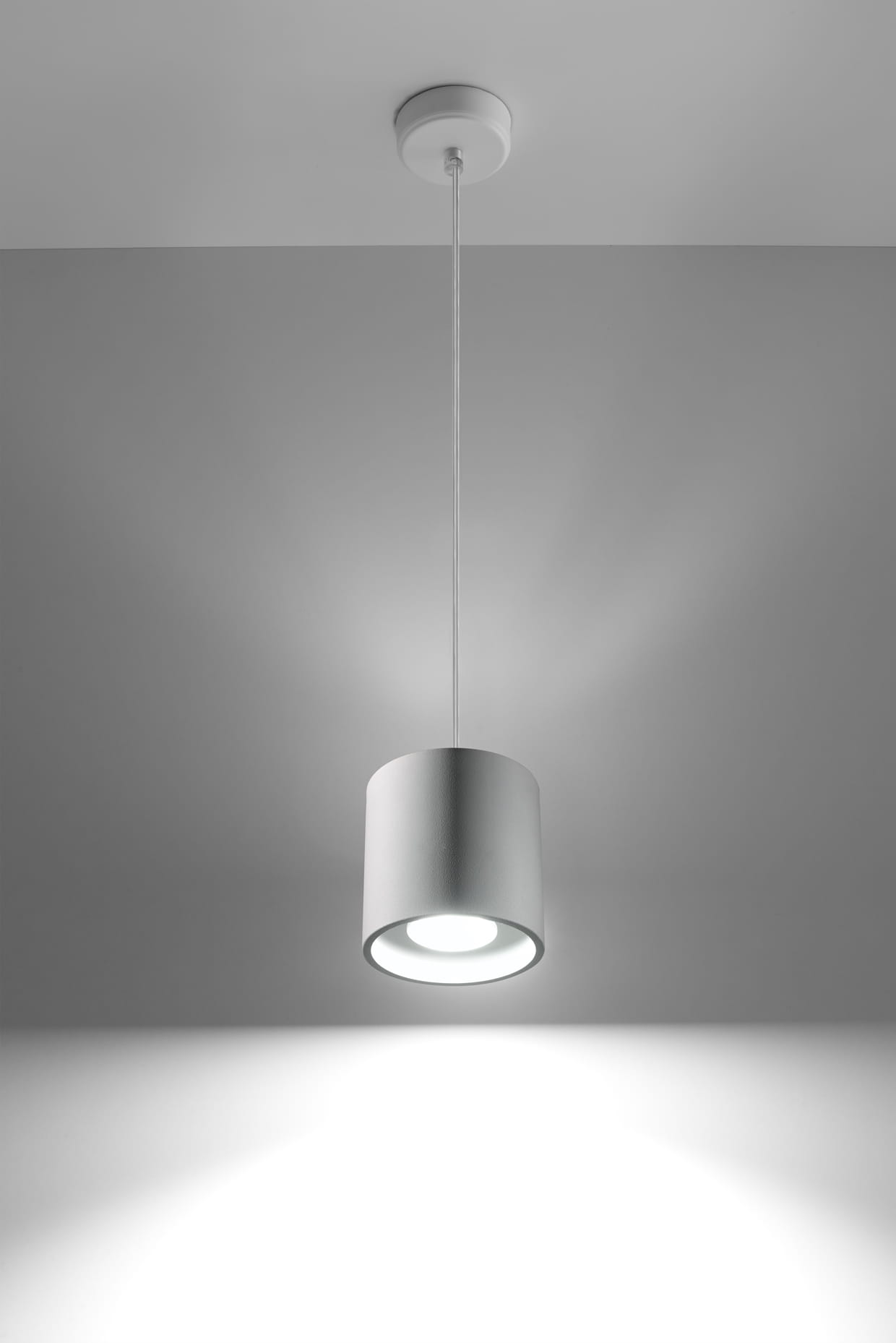 Biała lampa wisząca Orbis z cylindrycznym kloszem, zawieszona na cienkim przewodzie. Widok frontalny, podkreślający minimalistyczny design i równomierne oświetlenie otoczenia.