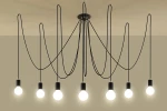 Lampa wisząca Edison 7-punktowa z czarnymi kablami i oprawkami, zawieszona na suficie. Każda z siedmiu żarówek ma okrągły kształt i emituje białe światło, tworząc minimalistyczny i nowoczesny wygląd na tle jasnej ściany.