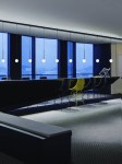 Lampa wisząca Track Ota I w kolorze czarnym, zawieszona na długich linkach, z sześcioma okrągłymi kloszami. Ujęcie z boku, w nowoczesnym wnętrzu z dużymi oknami. Widoczne krzesła w różnych kolorach, elegancki stół barowy.