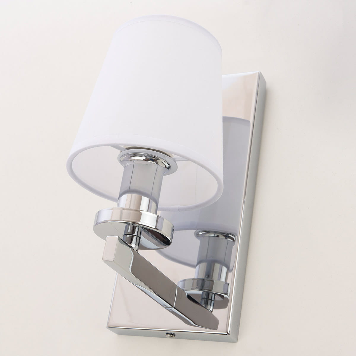 Kinkiet London 1-punktowy w kolorze chromu i białym, z okrągłym kloszem z materiału. Ujęcie z boku, ukazujące połyskującą, prostokątną podstawę i metalowy uchwyt. Minimalistyczny design, idealny do nowoczesnych wnętrz.