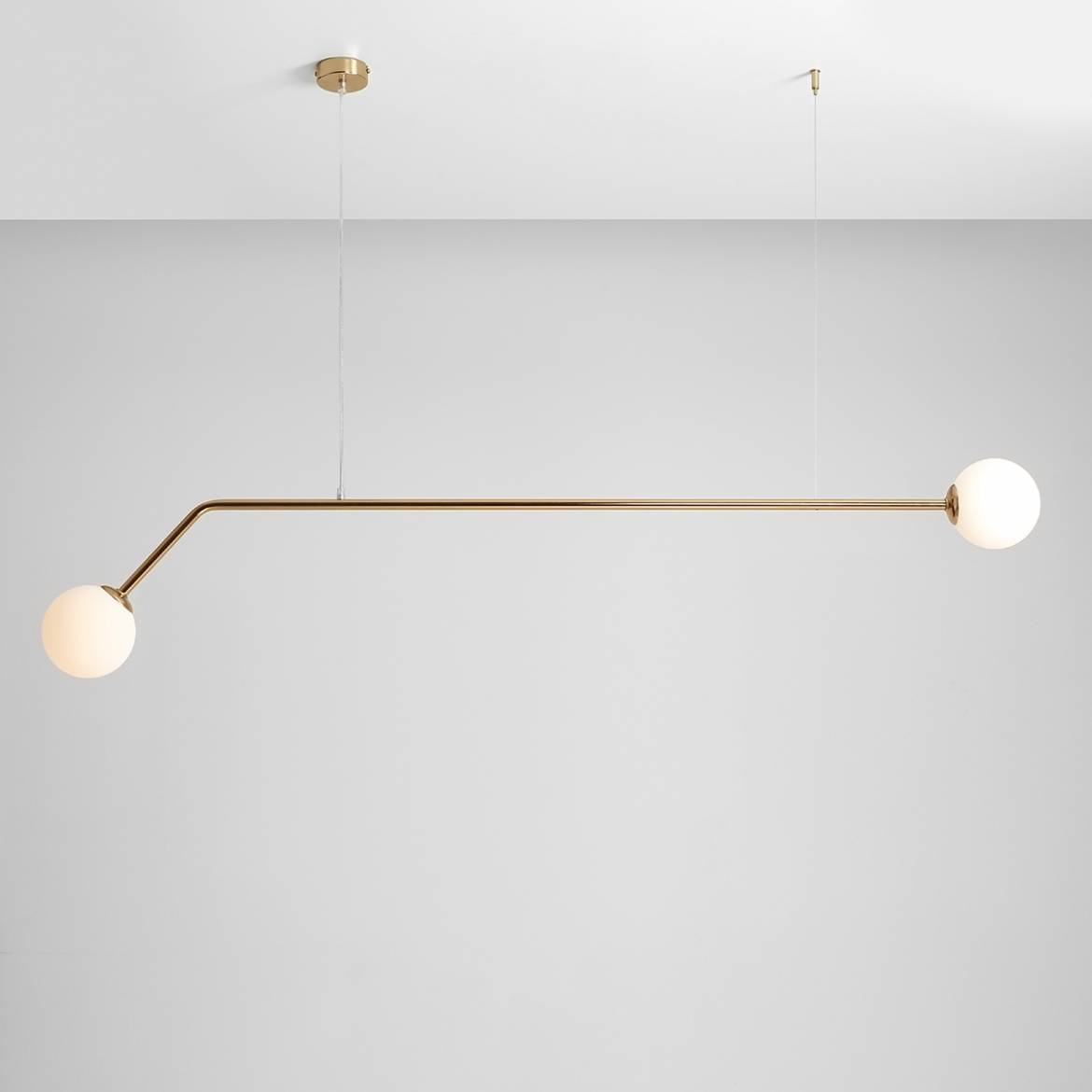Wisząca lampa Pure 2-punktowa w kolorze złotym z dwoma okrągłymi kloszami z białego szkła. Lampa ma prosty, poziomy kształt z jedną prostą rurką, zawieszoną na cienkich linkach, na jasnoszarym tle.