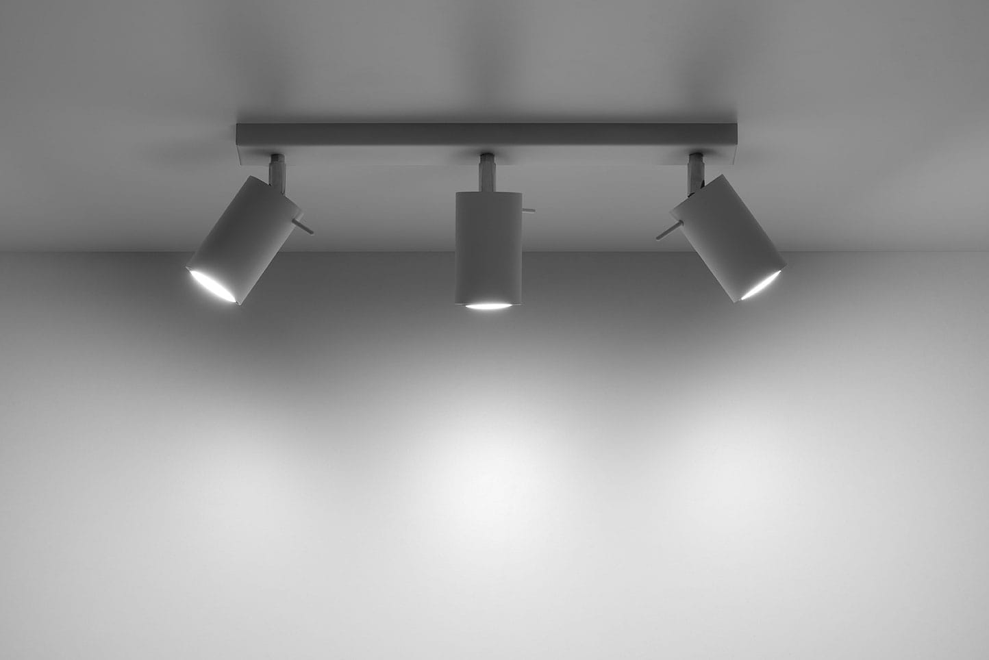 Biała lampa sufitowa 3-punktowa, zamontowana na prostokątnej podstawie, z trzema regulowanymi reflektorami. Reflektory mają cylindryczny kształt, emitując jasne światło. Tło jest jednolite i jasne, co podkreśla produkt.