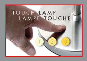 Lampa stołowa Touch Two z metalową podstawą, z widocznym przyciskiem dotykowym. Na podstawie znajdują się trzy okrągłe oznaczenia (1, 2, 3) do zmiany intensywności światła. Ręka dotykająca przycisku.