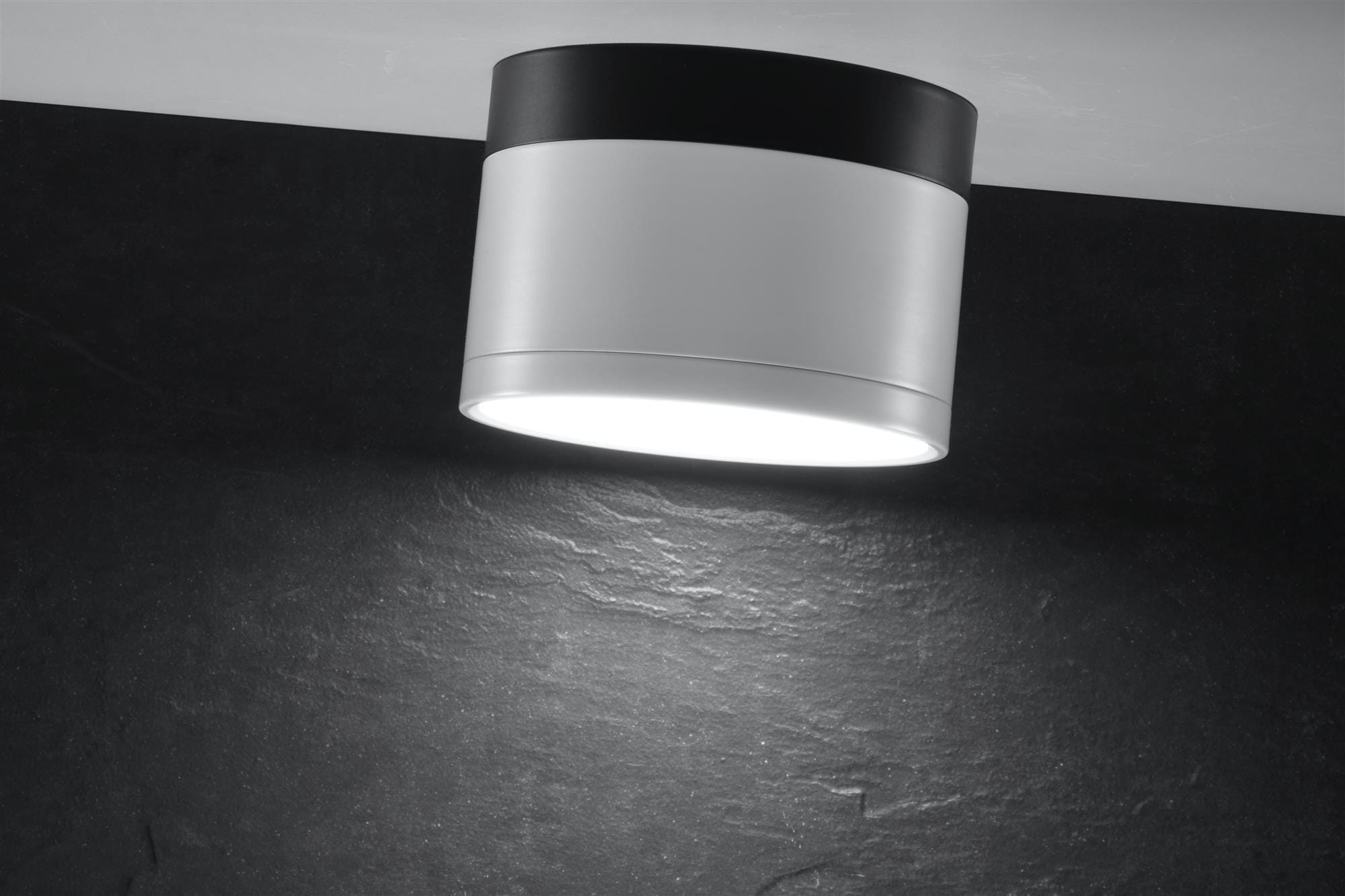 Lampa sufitowa Tuba LED 1-punktowa w kolorze białym z czarnym elementem, w formie cylindrycznej, zamontowana na suficie. Emituje jasne światło, z widoczną fakturą na tle ciemnej powierzchni.