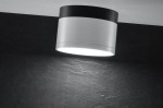 Lampa sufitowa Tuba LED 1-punktowa w kolorze białym z czarnym elementem, w formie cylindrycznej, zamontowana na suficie. Emituje jasne światło, z widoczną fakturą na tle ciemnej powierzchni.