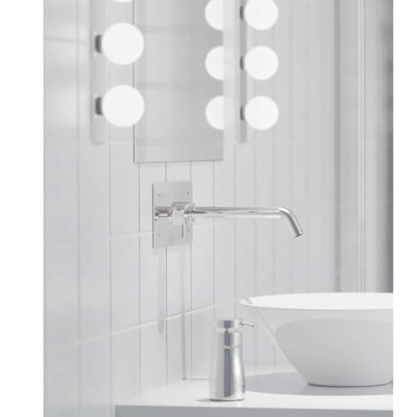 Kinkiet Brazos 3-punktowy w chromowanej obudowie, montowany na ścianie, z prostą, wygiętą końcówką. Widok na umywalkę i lustro z okrągłymi lampkami. Tło jasne, płytki ceramiczne.