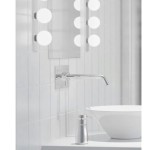 Kinkiet Brazos 3-punktowy w chromowanej obudowie, montowany na ścianie, z prostą, wygiętą końcówką. Widok na umywalkę i lustro z okrągłymi lampkami. Tło jasne, płytki ceramiczne.