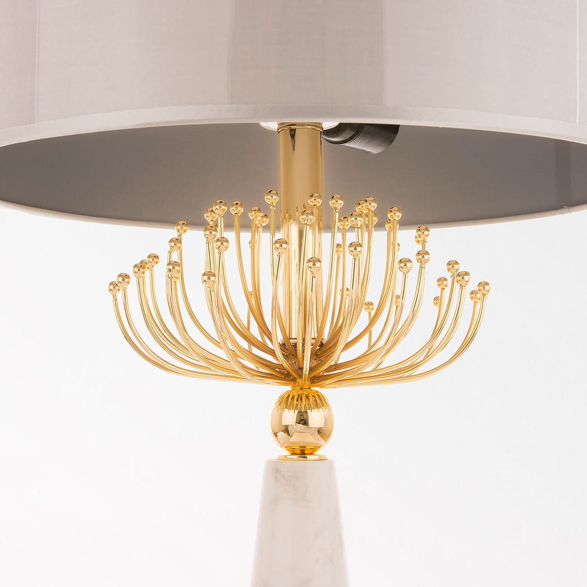 Lampa stołowa Cartagena 2-punktowa z metalową podstawą w kolorze złotym i marmurowym piedestale. Okrągły, szary klosz na górze, z dekoracyjnymi, zaokrąglonymi ramionami, które przypominają kwiat. Produkt w pozycji stojącej.