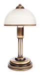 Lampa stołowa Sato O2088 L1 PAT w kolorze mosiądzu. Posiada szklany klosz o półkulistym kształcie i metalową podstawę z trzema cienkimi nogami. Ujęcie frontalne, ukazujące detale konstrukcji i fakturę materiałów.