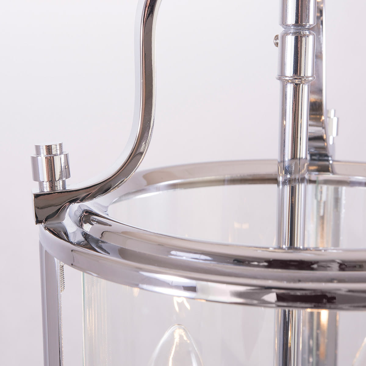 Lampa wisząca New York 3-punktowa, wykonana z chromowanego metalu i przezroczystego szkła. Ujęcie zbliżeniowe na detale mocowania i uchwytu. Nowoczesny design, idealna do eleganckich wnętrz.