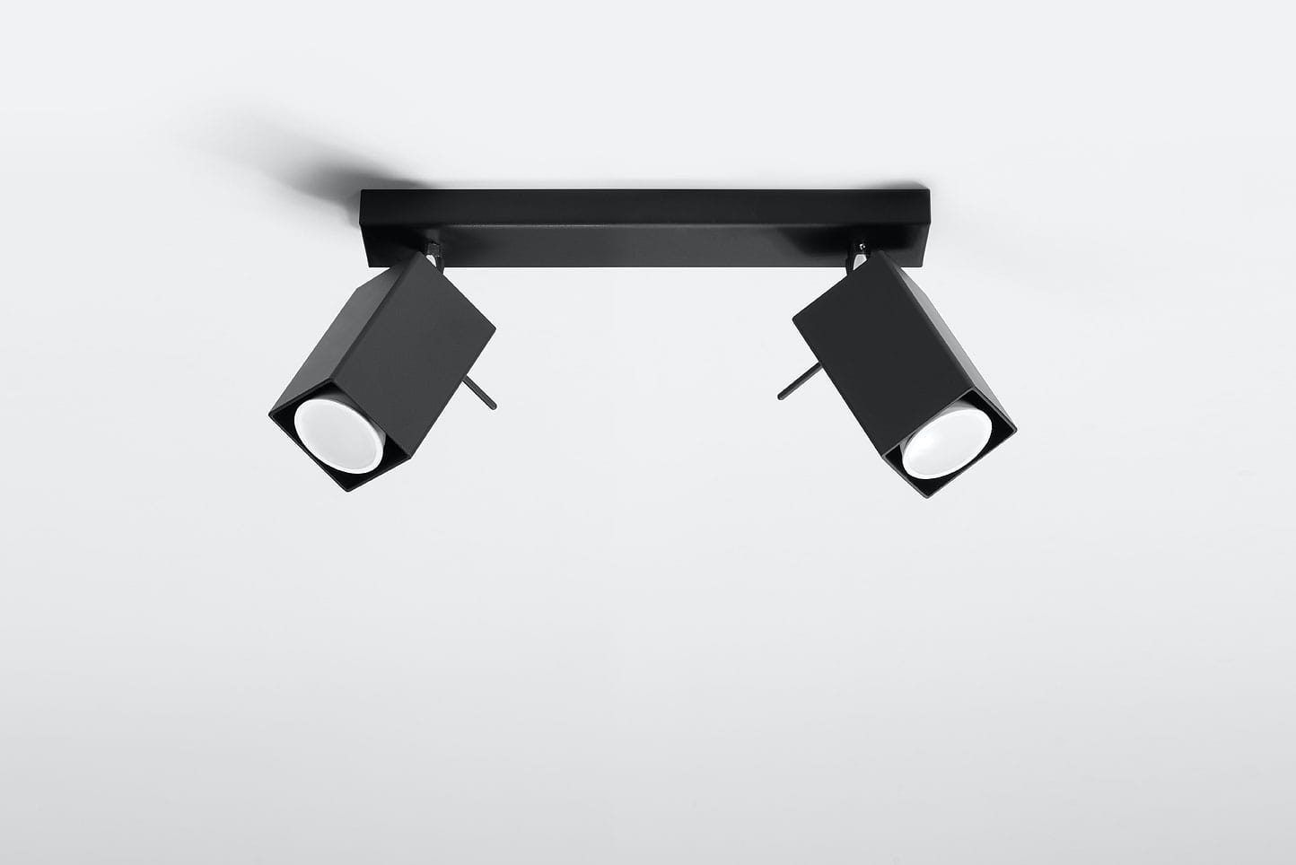 Czarna lampa sufitowa Merida, 2-punktowa, z dwoma prostokątnymi reflektorami. Ujęcie z dołu, pokazujące lampę zamontowaną na prostokątnej podstawie. Reflektory skierowane w przeciwnych kierunkach, z białymi kloszami. Tło jasne, jednolite.