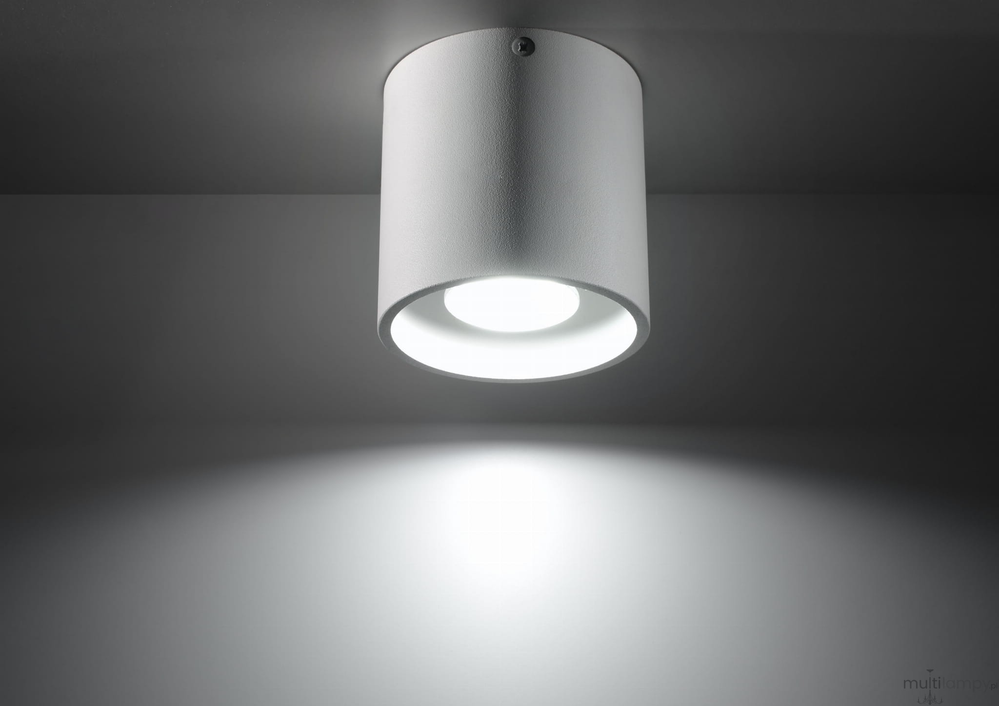 Biała lampa sufitowa 1-punktowa Orbis SL.0021, cylindryczny kształt, matowa powierzchnia. Widok z dołu, skierowana w dół, emitująca jasne światło. Proste tło podkreślające minimalistyczny design.