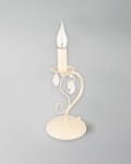 Lampa stołowa Velio 1-punktowa w kolorze kremowym, z metalową podstawą w kształcie okręgu. Wyposażona w przezroczystą żarówkę w kształcie płomienia oraz dwa kryształowe zwisy. Ujęcie z boku, na jednolitym tle.