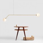 Lampa wisząca 2-punktowa Pure w złotym kolorze, z długim, prostokątnym ramieniem i dwoma okrągłymi kloszami z białego szkła. Produkt zawieszony na cienkim kablu, w tle drewniany stół i kawałek drewna. Tło jasnoszare.
