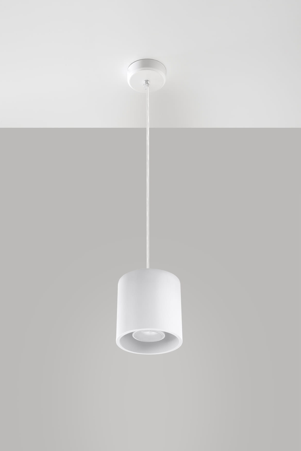 Lampa wisząca Orbis 1-punktowa w kolorze białym, okrągła, z matowym wykończeniem. Zawieszona na cienkim, białym przewodzie, z prostym, okrągłym kloszem. Zdjęcie wykonane z góry, na jednolitym szarym tle.